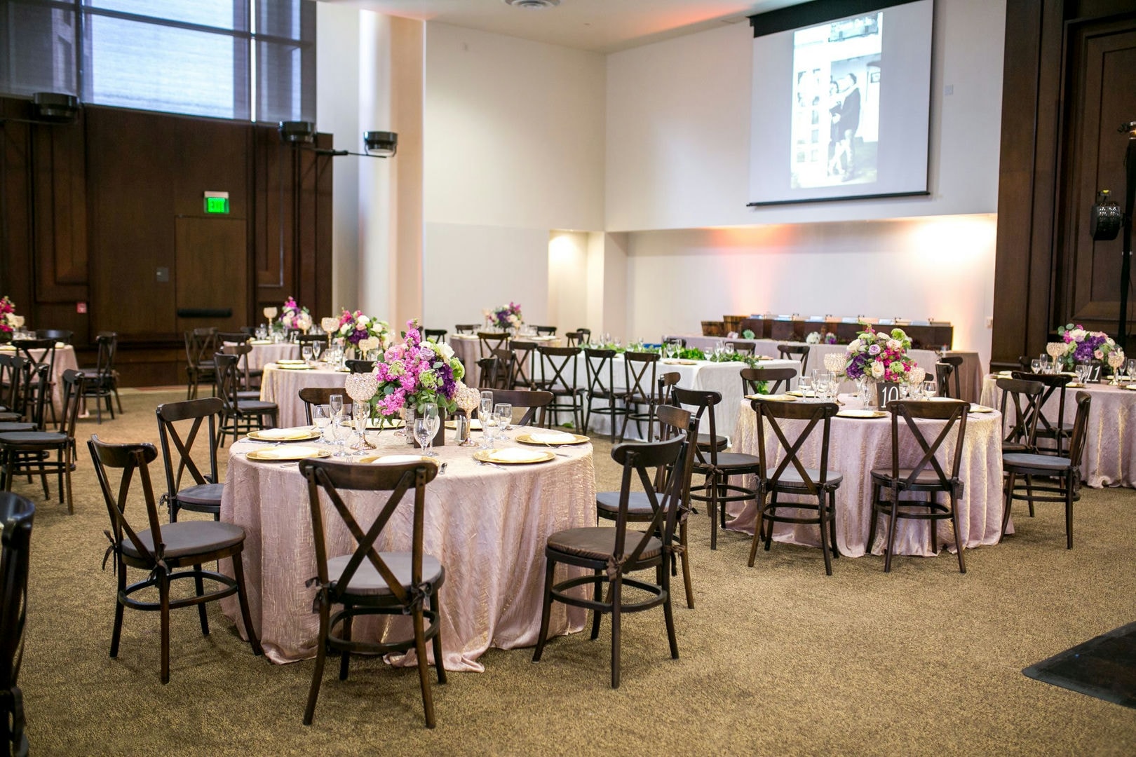 A large room with round tables, chairs, and floral centerpieces.