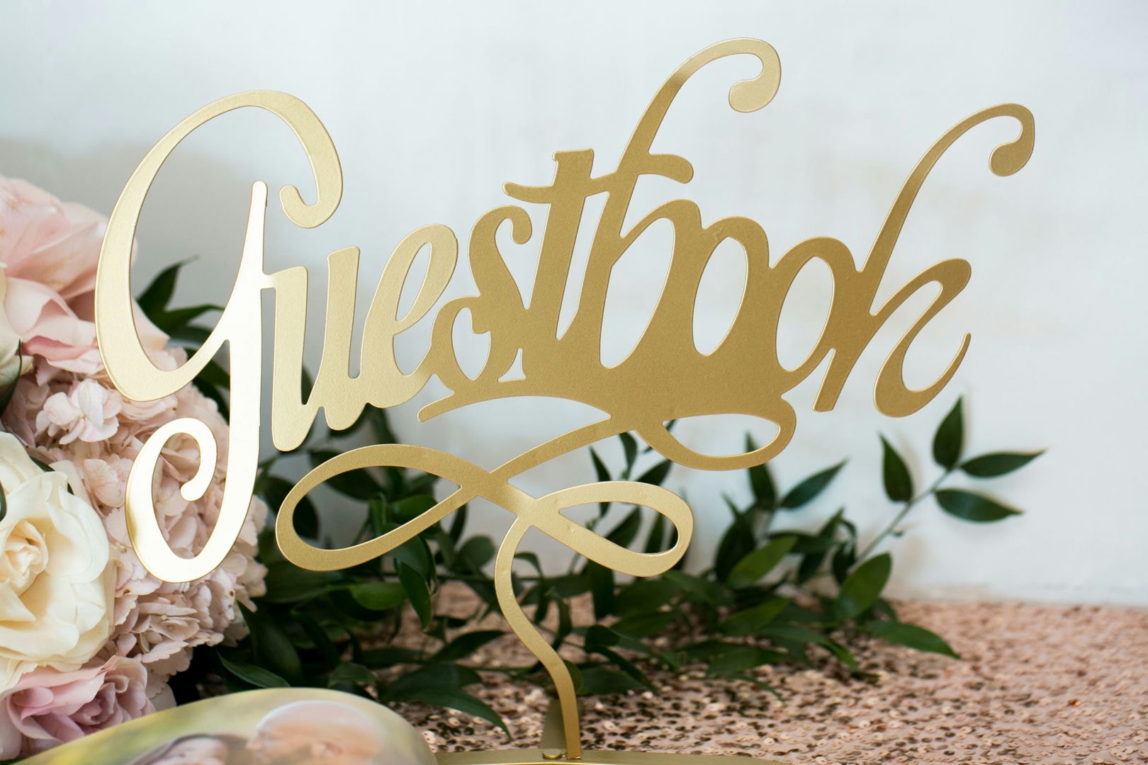 Gold "Guest Book" sign, pink flowers, and greenery.