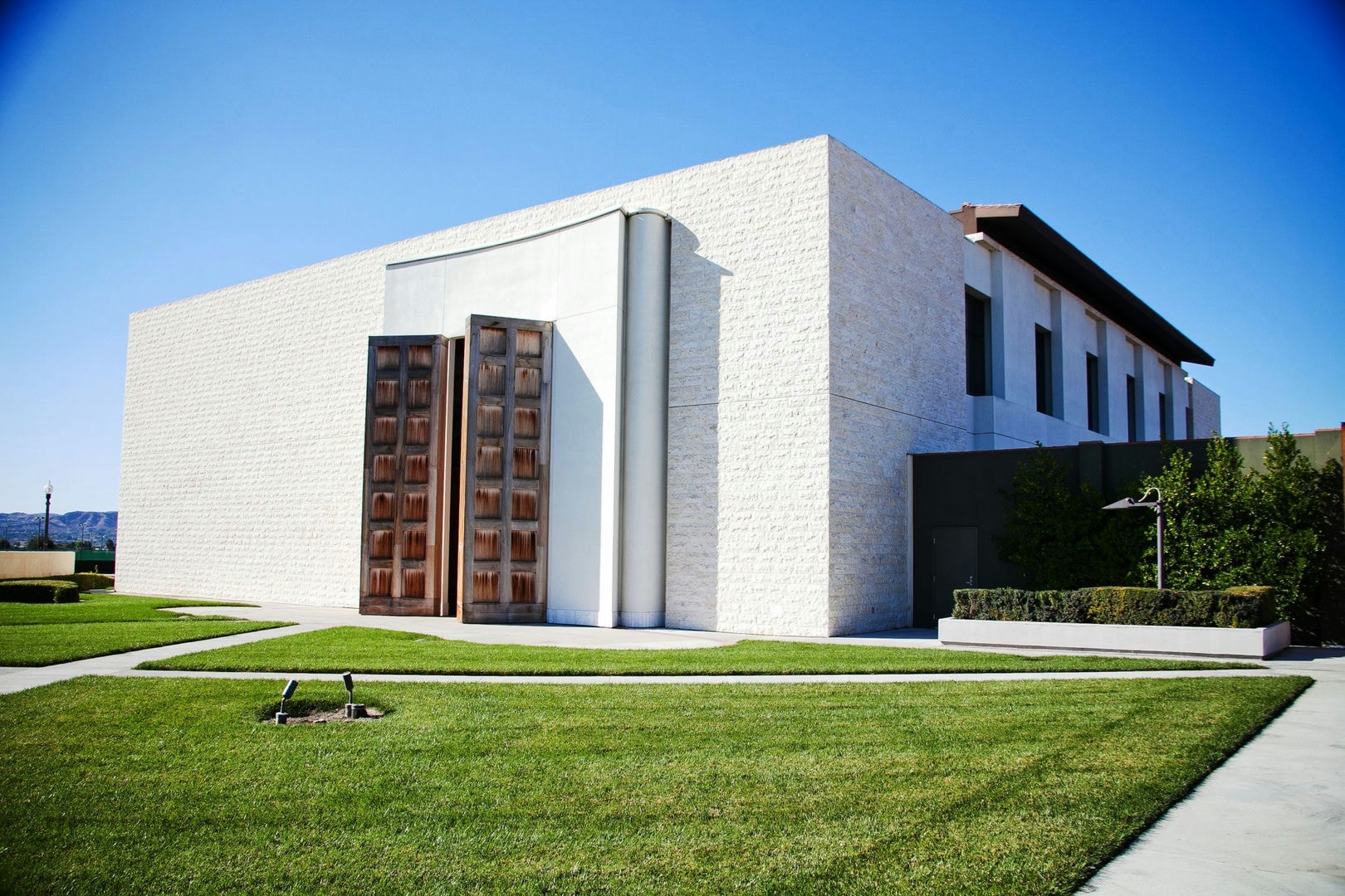 A light-colored building with large wooden doors, surrounded by grass and landscaping.