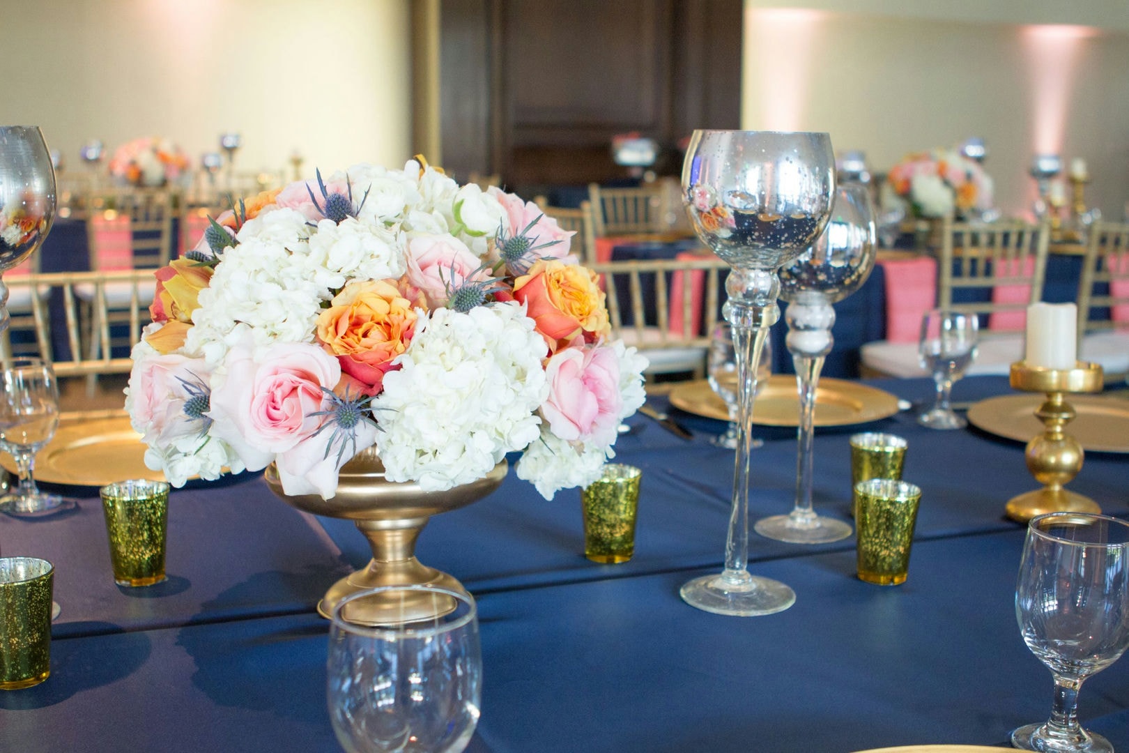 A long table set for a banquet, with gold chairs and a navy blue tablecloth. Pink accents are on the table.