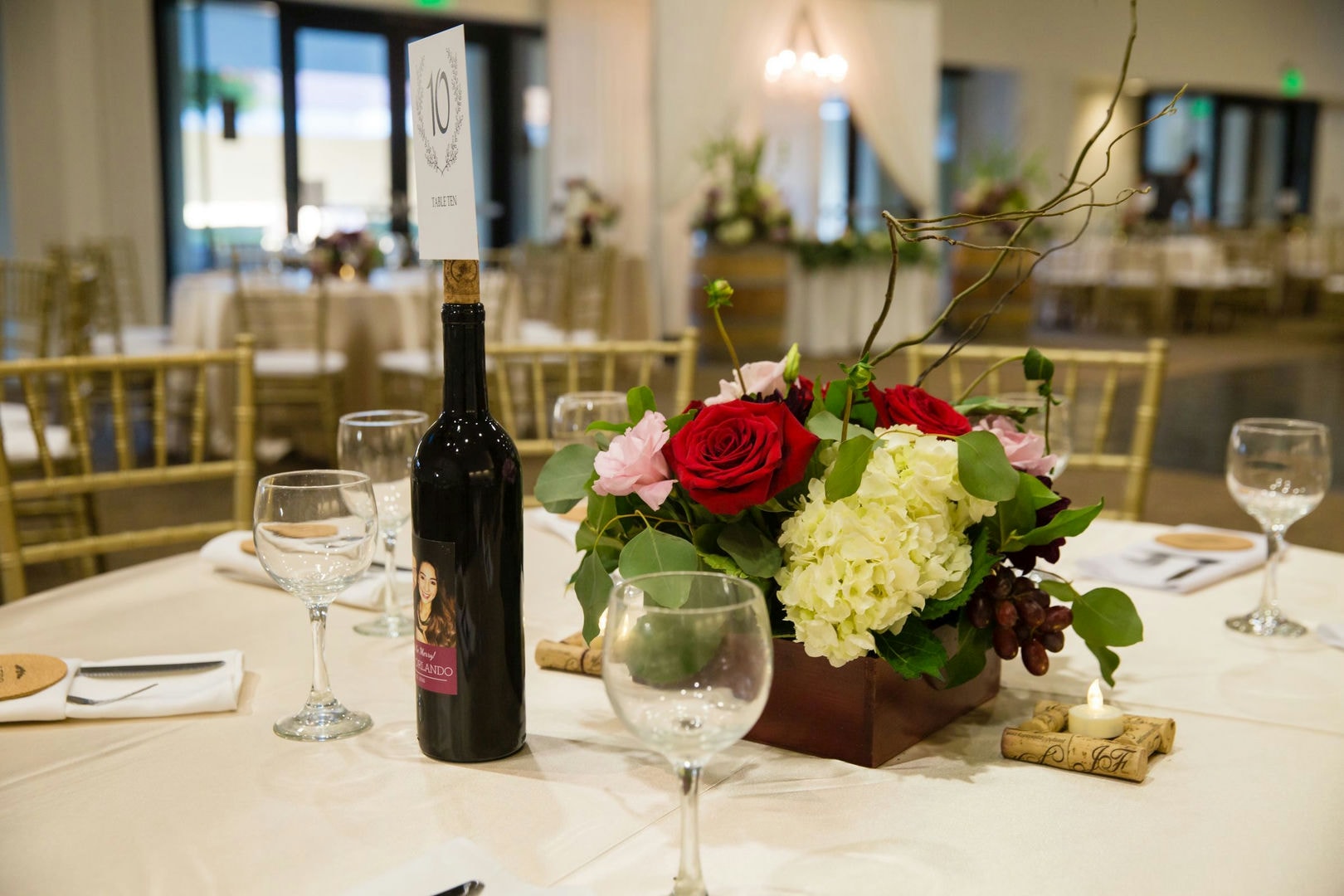 A round table with a centerpiece of flowers, wine bottles, and glasses.