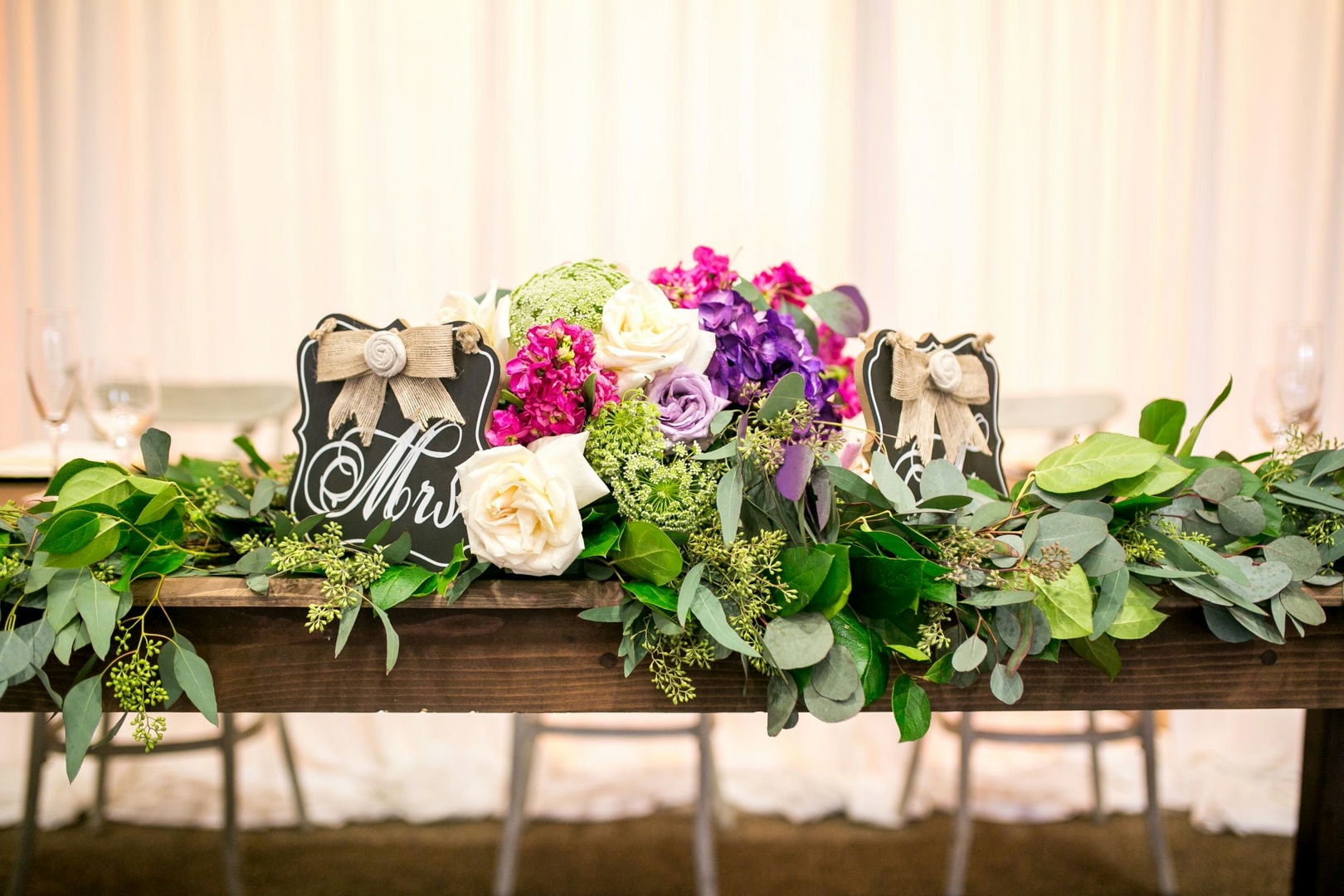 A wooden table decorated with flowers, greenery, and Mr./Mrs. signs.