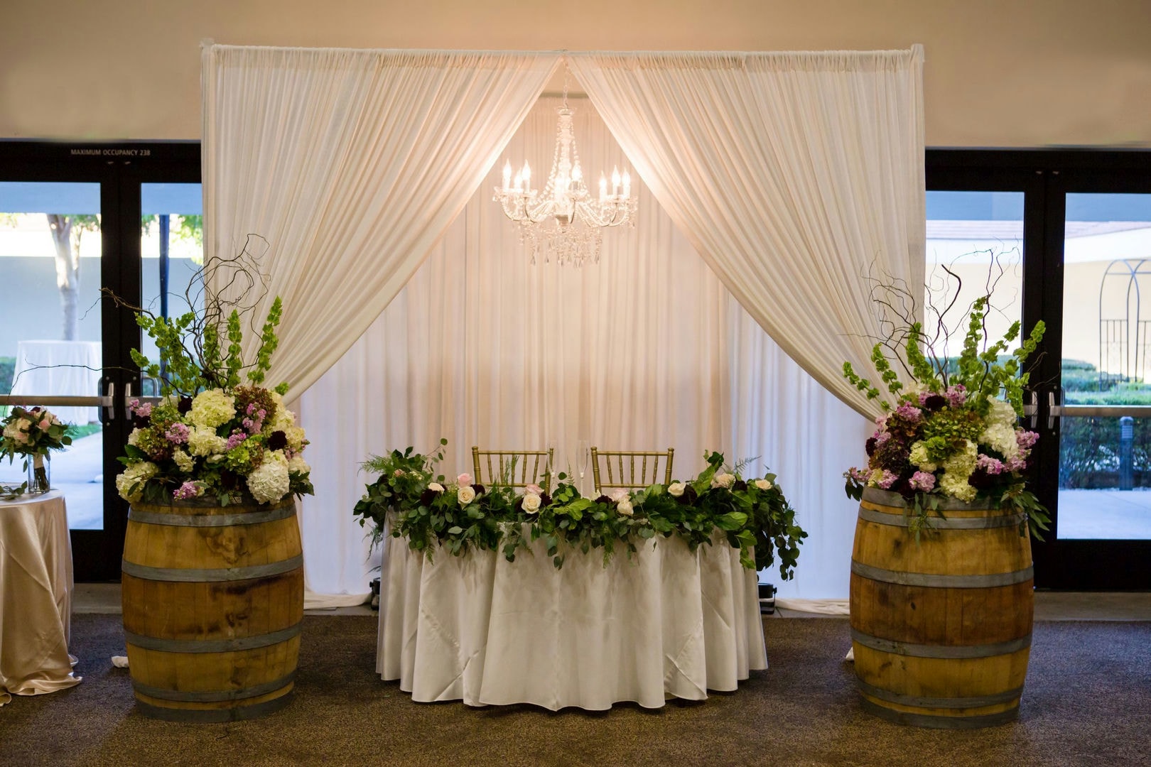 A decorated table setting with flowers and a chandelier. Two chairs and a round table are visible.