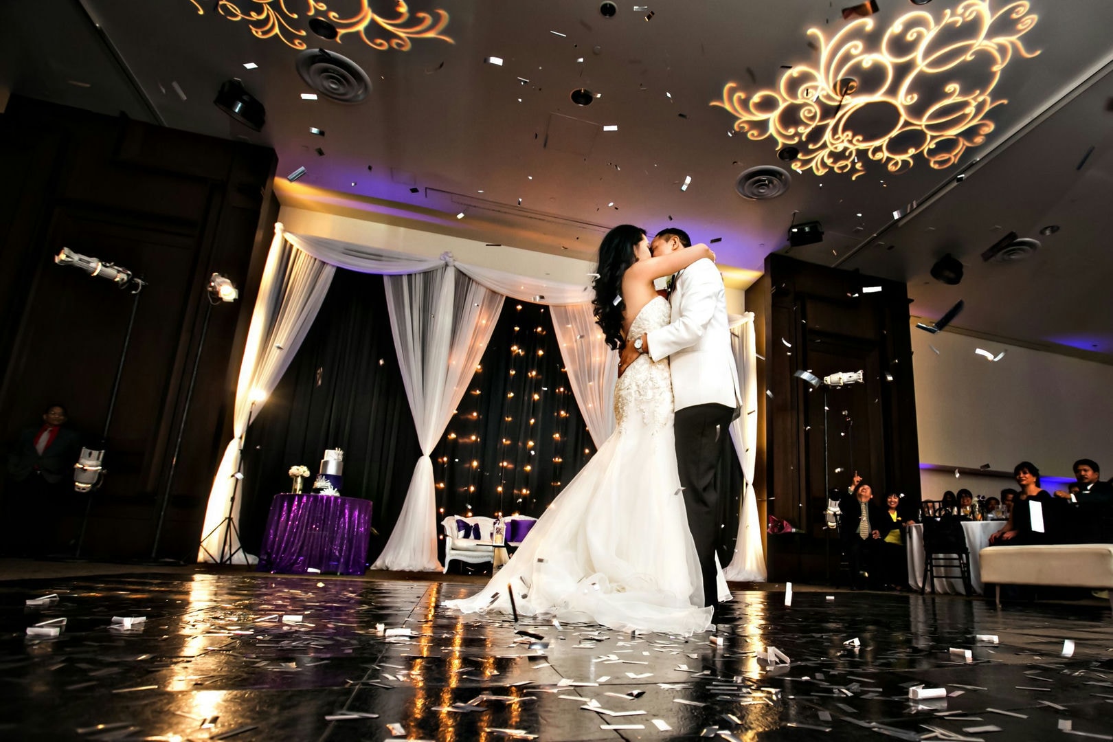 A bride and groom are dancing on a dance floor, confetti is falling, and there are people watching.