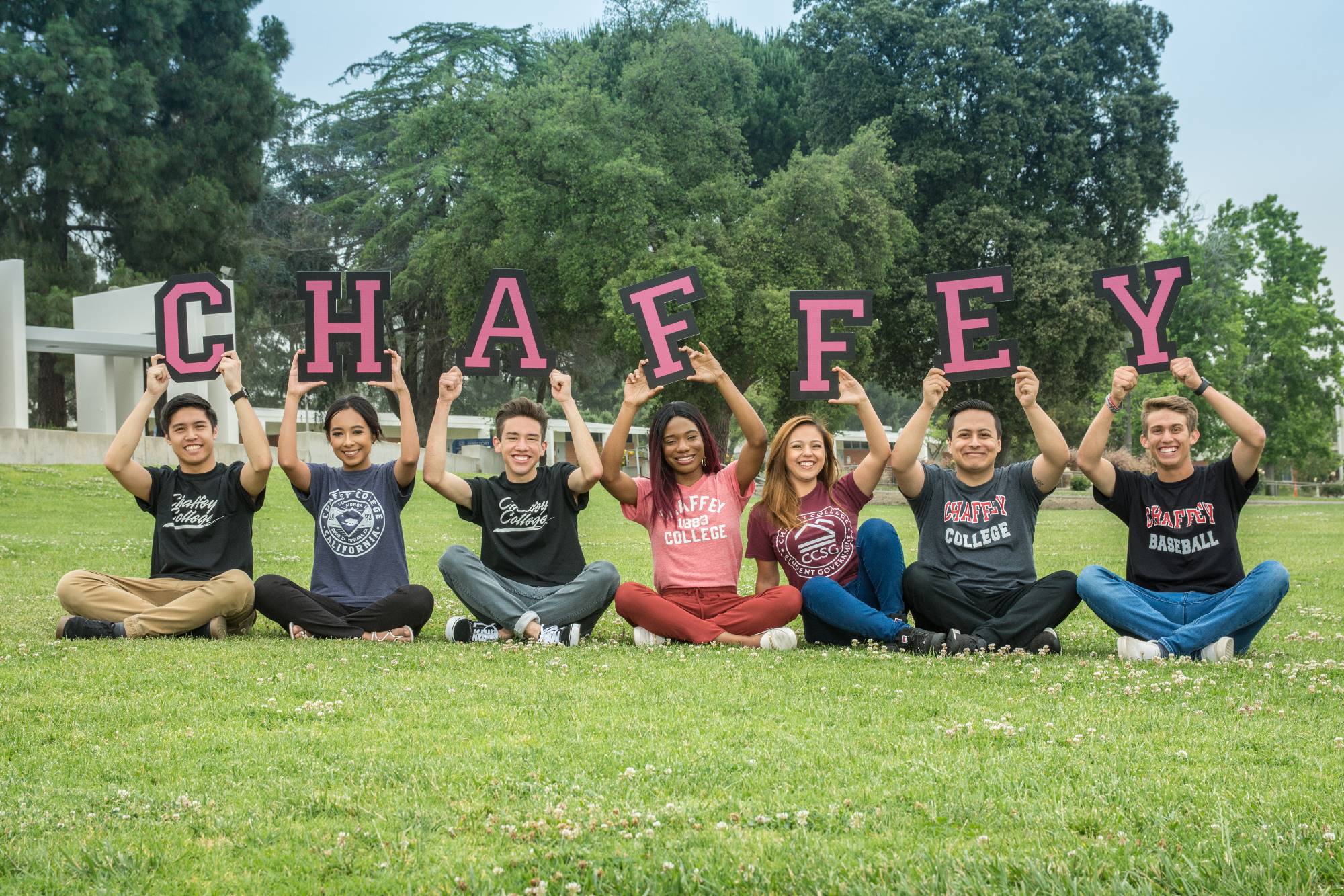 Students hold up the letters "Chaffey" as they sit on the grass on campus.