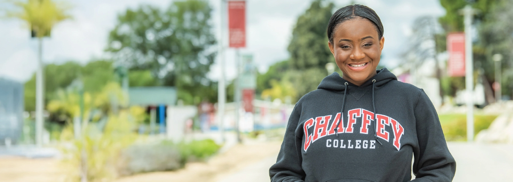 Smiling student wearing Chaffey College sweatshirt, with greenery in the background. Text on the sweatshirt reads: CHAFFEY COLLEGE.