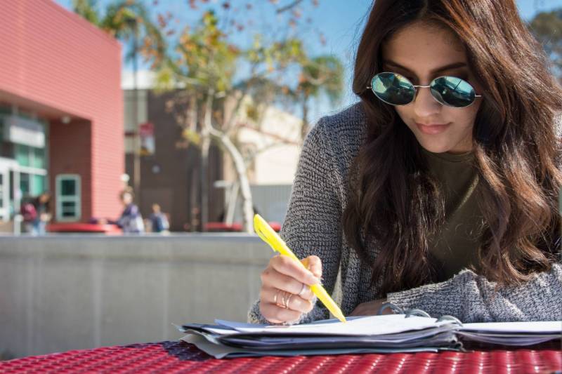 A student wearing sunglasses highlights some notes at the Fontana campus.