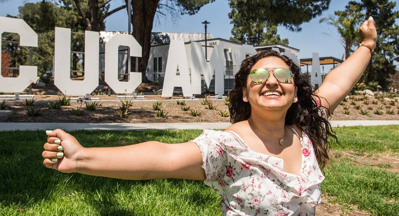 A student smiles and spreads her arms in front of the Cucamonga sculpture at Chaffey College.